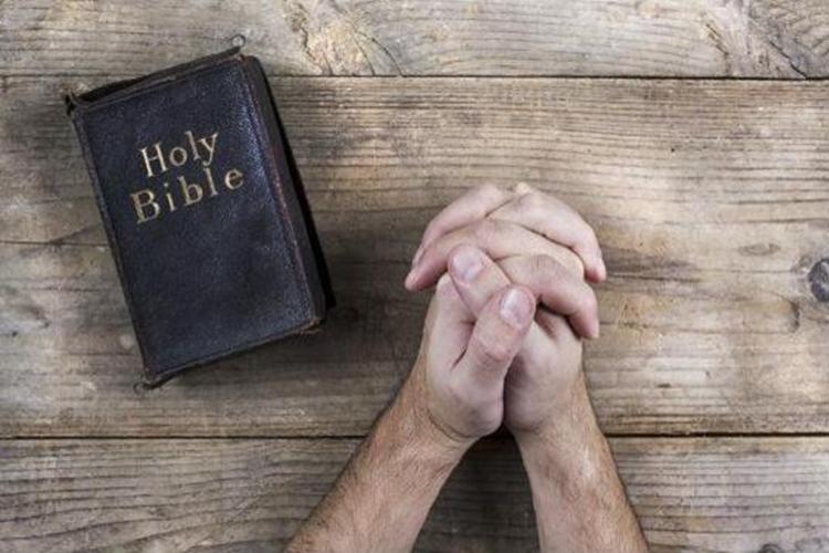 A picture of a man praying with the Bible next to him