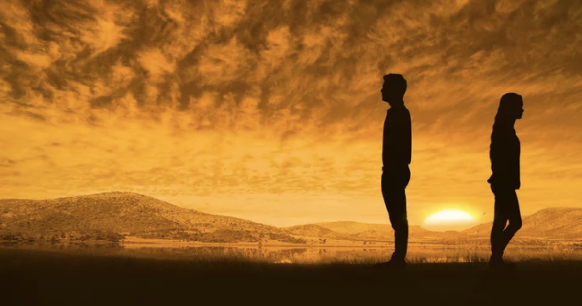 A couple stands silently with their backs to each other.