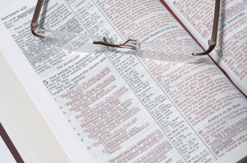 A pair of glasses is on the page Sermon on the Mount of an opened bible.
