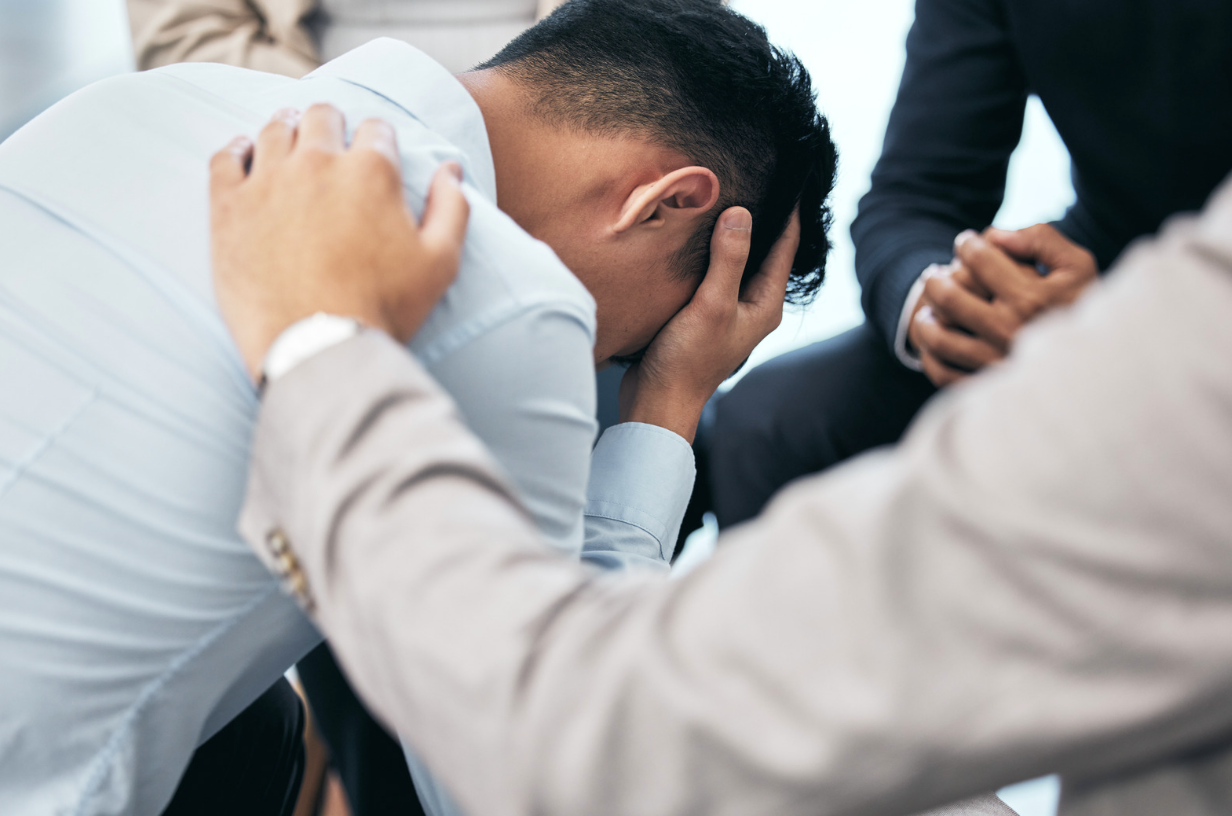 A supporting hand comforts a man suffering from mental health.