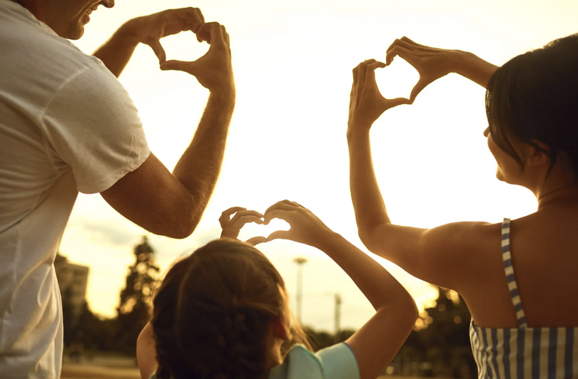 A picture of a family of three posting love gestures to each other