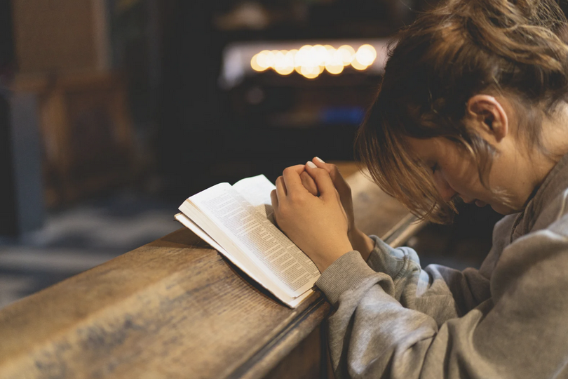 A Christian woman prays with an open Bible.
