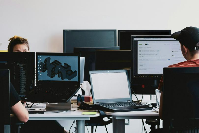 A man in a black shirt sits on a chair in front of computer monitors.