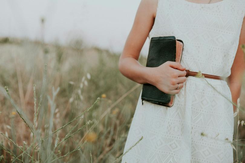 A woman in a white dress holds a book.