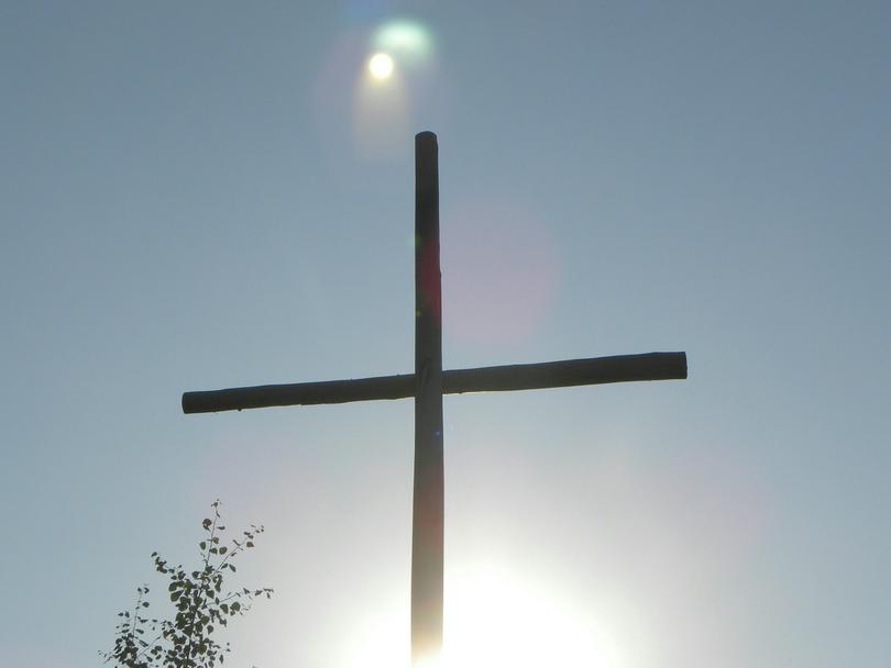 A cross on top of a hill with the sun shining behind it.