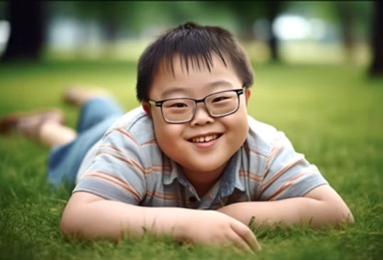 A kid with Down Syndrome lied on the grass happliy on an unknown day.