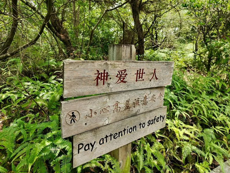 Three wooden plaques display the message “For God so loved the world” along with a bilingual reminder: “Pay attention to safety” at Li Lang Holy Mountain Park in Shenzhen, Guangdong.