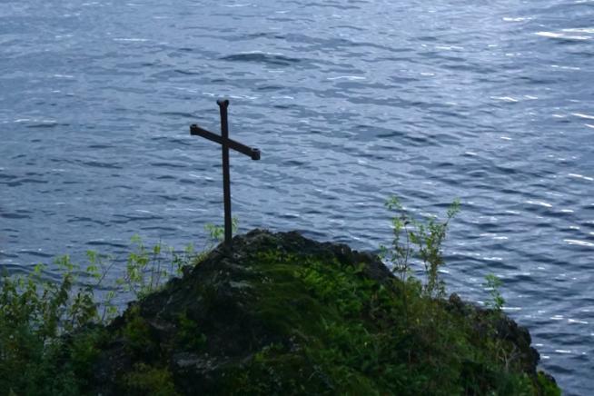 A cross sits on a hill overlooking a body of water.