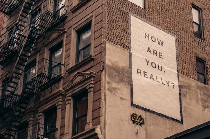A big poster with "HOW ARE YOU REALLY?" was posted on a brown concrete building.