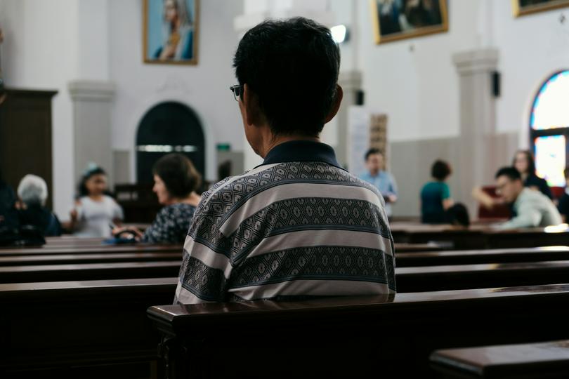 A man sits in a church on an unknown day.