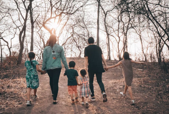 A family walks on a brown dirt road on daytime.