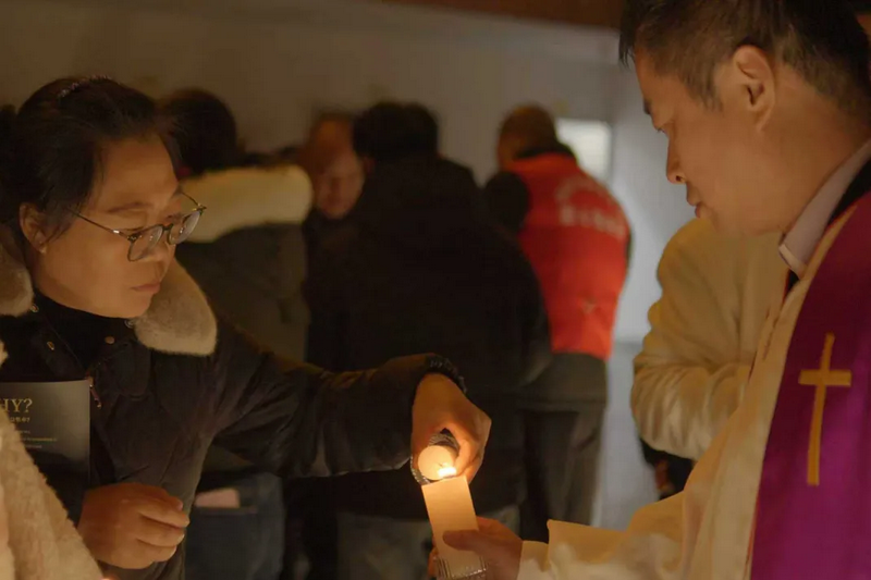 The light of the candle was passed between a minister and a congregant during the Christmas tree lighting ceremony at Changshu Church in Suzhou, Jiangsu Province, on December 5, 2025.