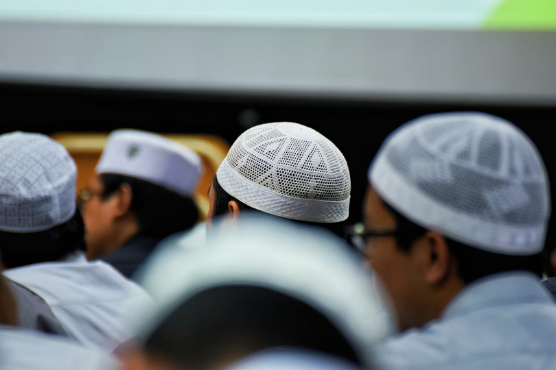 Muslim men wear traditional white skullcaps during a religious gathering on an unknown day.