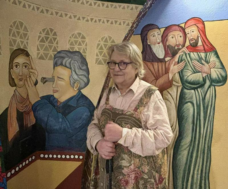 Helena Nikkanen and her painting work of a woman looking at the speck of sawdust in a younger sister's eye through the plank in her own eye at the Church of the Resurrection at the Anaphora Retreat Center, Wadi El Natrun, Egypt