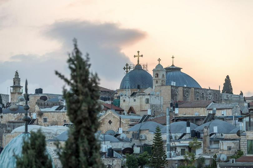 A panoramic view of the rooftops of the Old City of Jerusalem, with the prominent domes of the Church of the Holy Sepulchre in the background