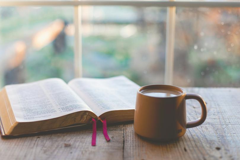 An open Bible and a cup of coffee by the window