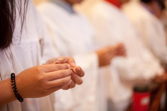 A member holds the bread and cupof wine in her hands