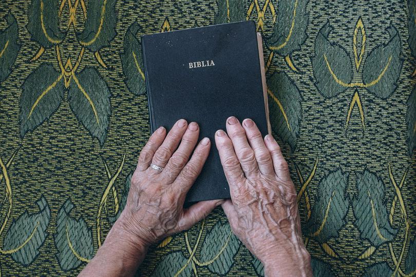An elderly person places his hands on the Bible.
