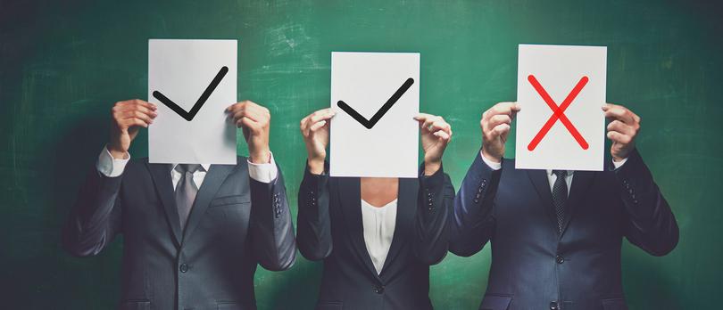 Three workplace people hold signs that say, yes or no.