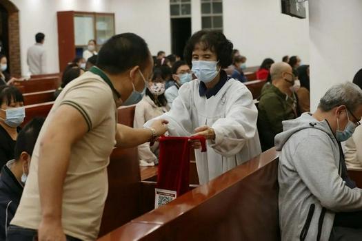 A male Christian put some money into a red offering bag in a Thanksgiving Charity Gala in Guangxiao Church, Guangzhou, Guangdong, on November 28,2021.